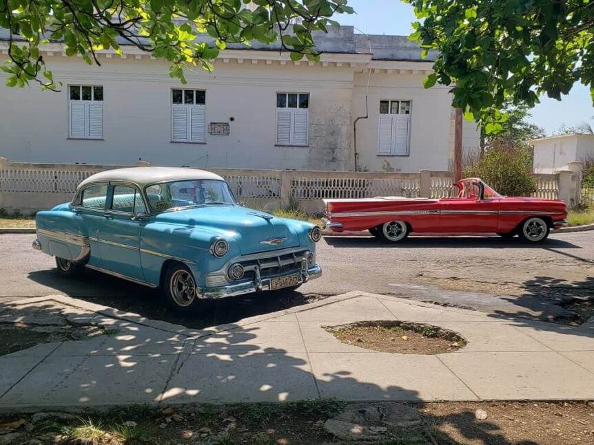 A vibrant scene of a sky blue Chevy hardtop '53 and a red convertible Impala '59 driving through the historic streets of Havana, Cuba. The image captures the essence of a classic car tour in Havana, showcasing iconic landmarks such as El Capitolio and the Malecón, with the beautiful colonial architecture in the background