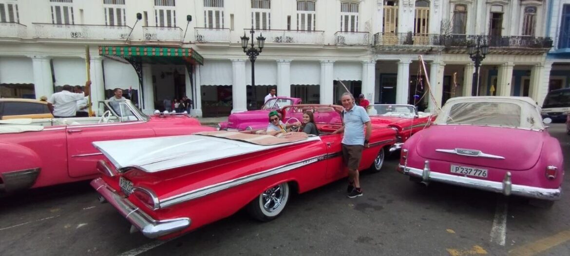 A red vintage convertible with a tourist group in front of colonial buildings during classic car tours Havana in Cuba.