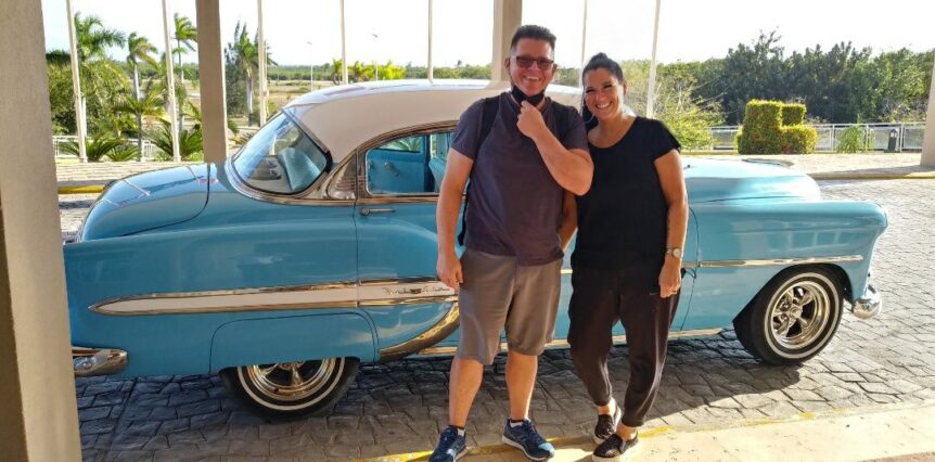 Happy travelers in front of a classic vintage blue car used for private transfers from Havana Airport to Varadero