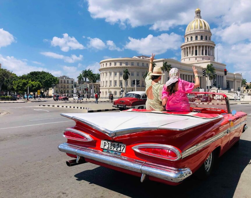 A vibrant scene of a classic American car with air conditioning driving along the Malecón in Havana, Cuba, with the El Capitolio building and colonial architecture in the background. The image captures the essence of a day trip from Varadero to Havana, showcasing the classic car, beautiful architecture, and vibrant city atmosphere.