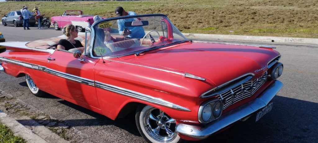 Red 1950s classic convertible with passengers on a scenic Havana street