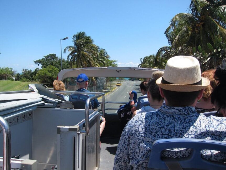 Varadero double decker hop-on hop-off tourist bus driving along the resort area with clear blue skies and palm trees in the background